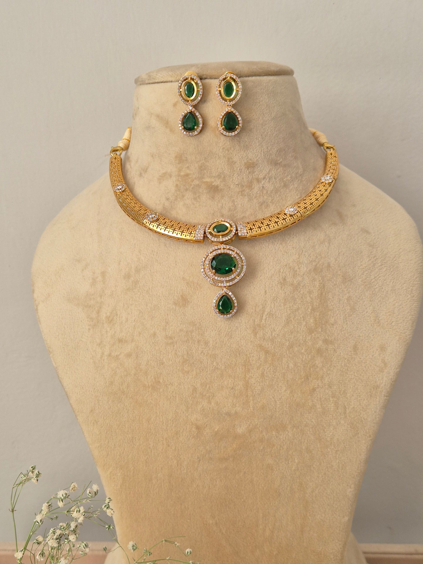 Gold choker necklace with a central green gemstone pendant and matching earrings by naitri.in