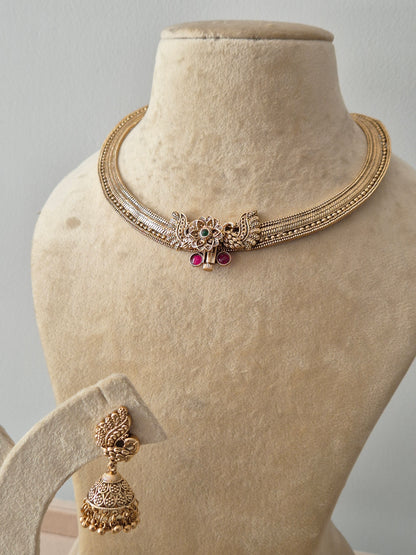 Traditional Indian festive jewelry set including a textured gold collar necklace and hanging Jhumka earrings with pink bead droplets by naitri.in