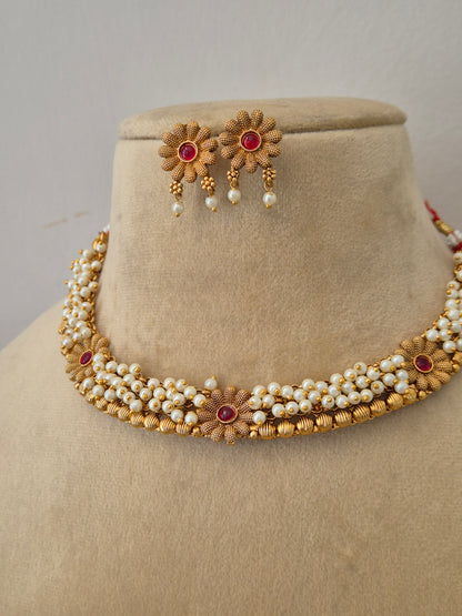Handcrafted brass alloy choker made of intricate pearl strands and ruby-red floral embellishments,  delicate gold flowers by naitri.in