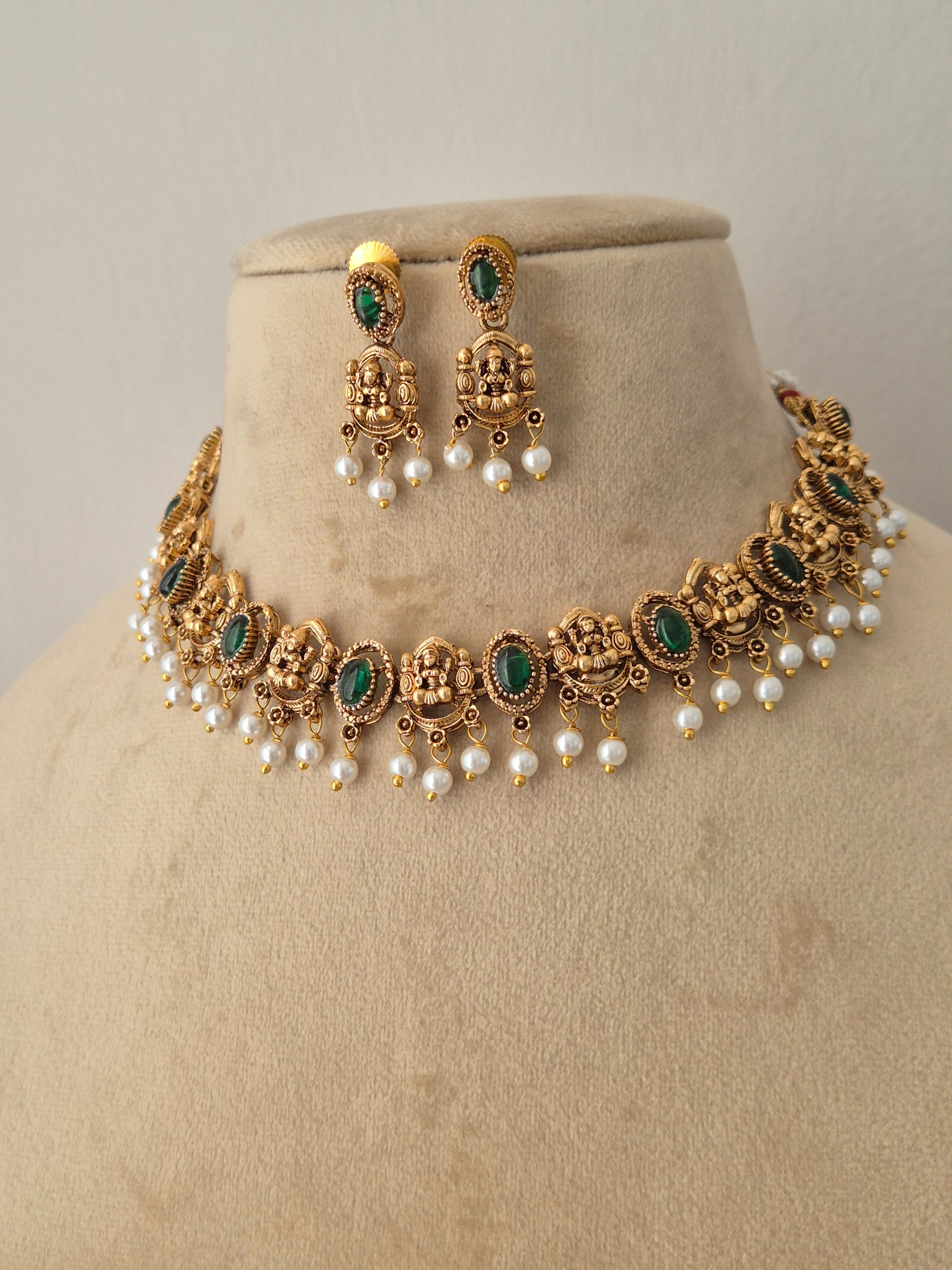 Antique gold-plated ethnic choker set featuring intricate Indian artisanal metalwork, oval-cut green stones, and delicate hanging white pearls, shown alongside matching dangle earrings. by naitri.in