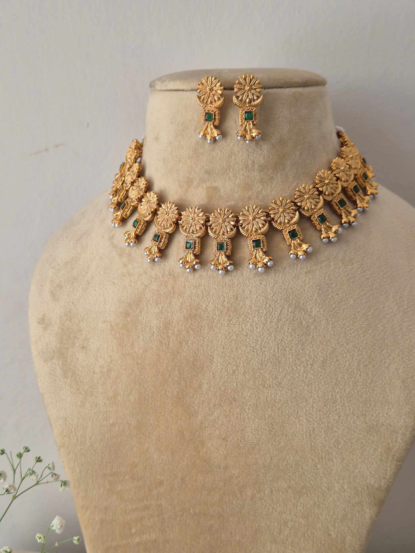 Gold-plated ethnic choker set featuring intricate textured circular engravings, small green stone embellishments, and delicate white hanging pearls by naitri.in