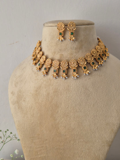 Gold-plated ethnic choker set featuring intricate textured circular engravings, small green stone embellishments, and delicate white hanging pearls by naitri.in