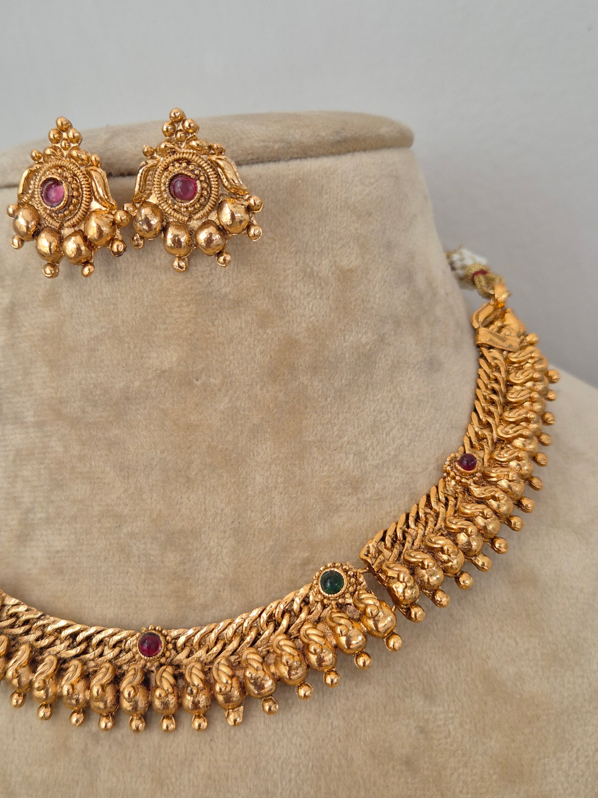 Traditional Indian antique-finish brass necklace set showcasing elaborate textured ridge motifs, small colorful gemstone embellishments, and delicate hanging gold beads from the Naitri Golden Jewellery collection by naitri.in