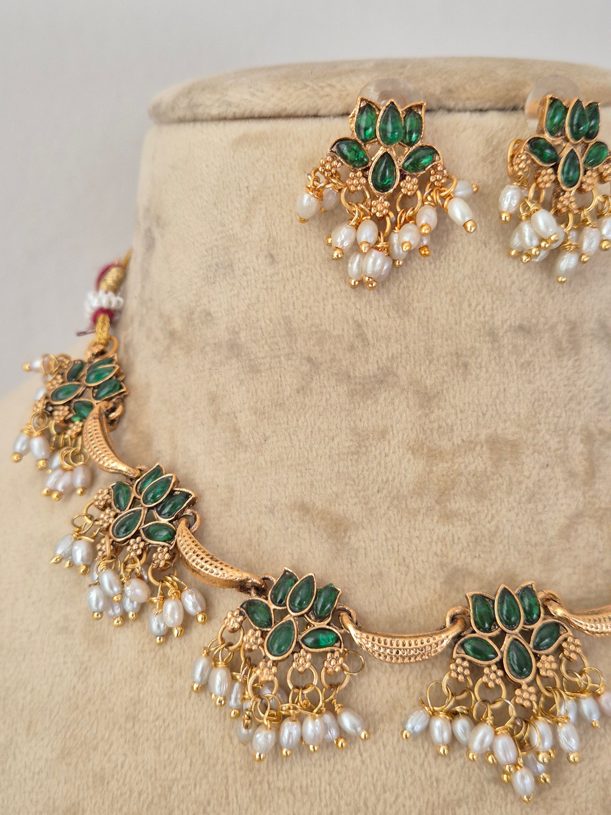 Gold-toned traditional jewelry set featuring a necklace and matching earrings, embellished with green stones and white pearl-like beads, by naitri.in