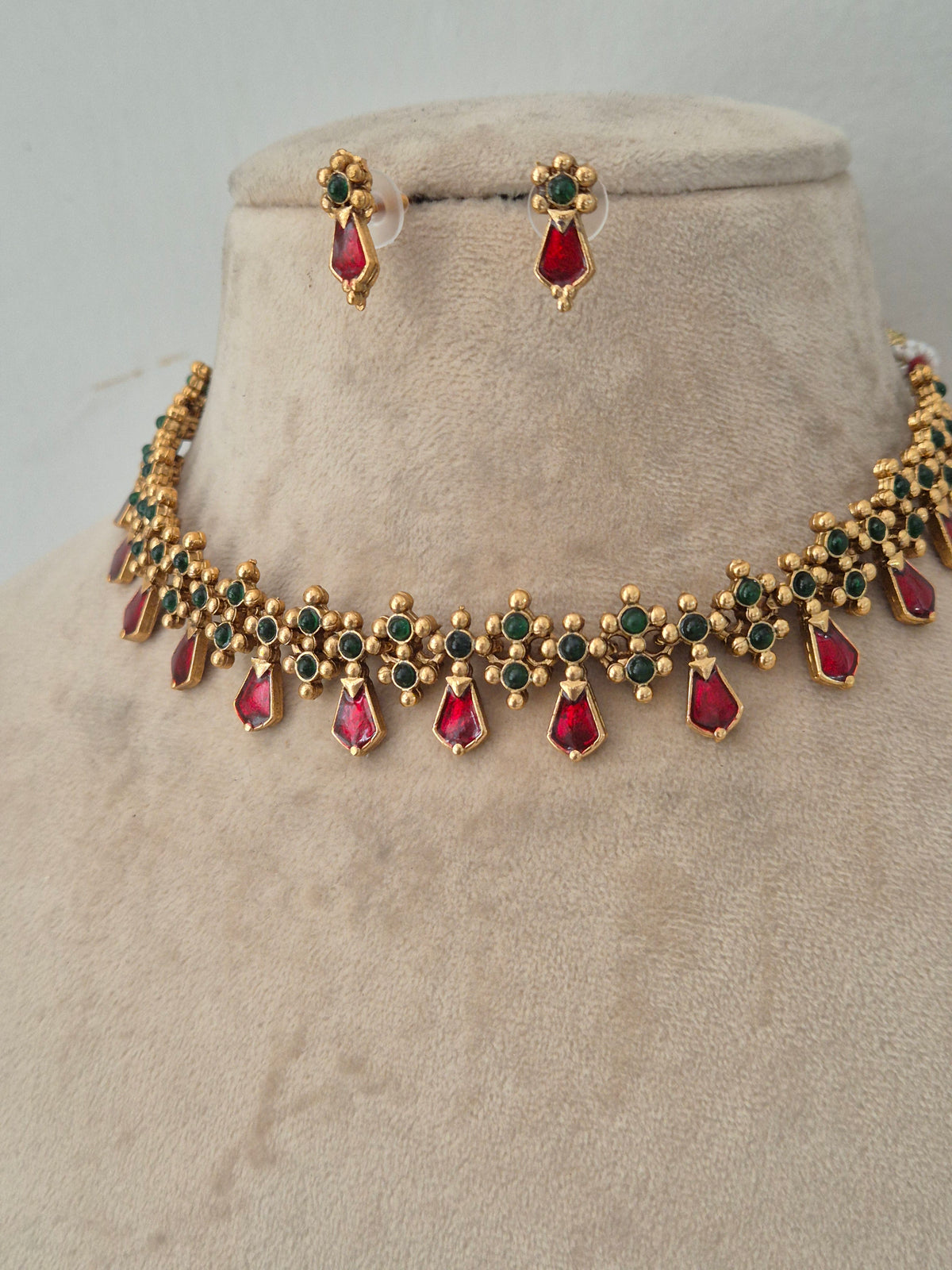Gold choker necklace with red and green stone detailing and matching stud earrings by naitri.in