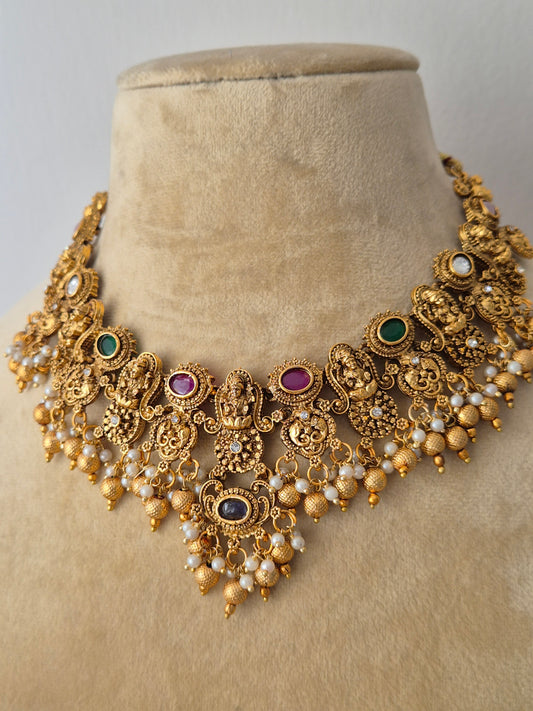 Traditional Indian antique-finish brass necklace set showcasing elaborate floral and deity metalwork engravings, colorful gemstone accents, and delicate dangling gold beads from the Naitri Golden Jewellery collection by naitri.in