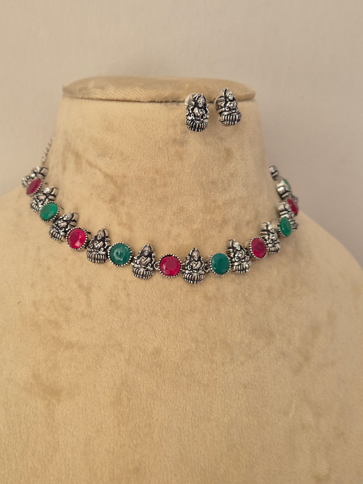 A silver-toned jewelry set featuring a necklace and matching earrings with small metallic motifs and round green and pink stones by naitri