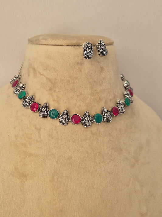 A silver-toned jewelry set featuring a necklace and matching earrings with small metallic motifs and round green and pink stones by naitri
