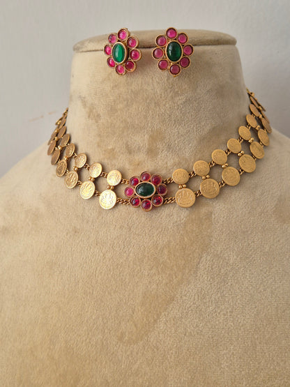 Gold-plated ethnic choker set composed of two rows of textured circular discs and a central ruby-pink and emerald-green gemstone flower, shown with matching flower stud earrings by naitri.in