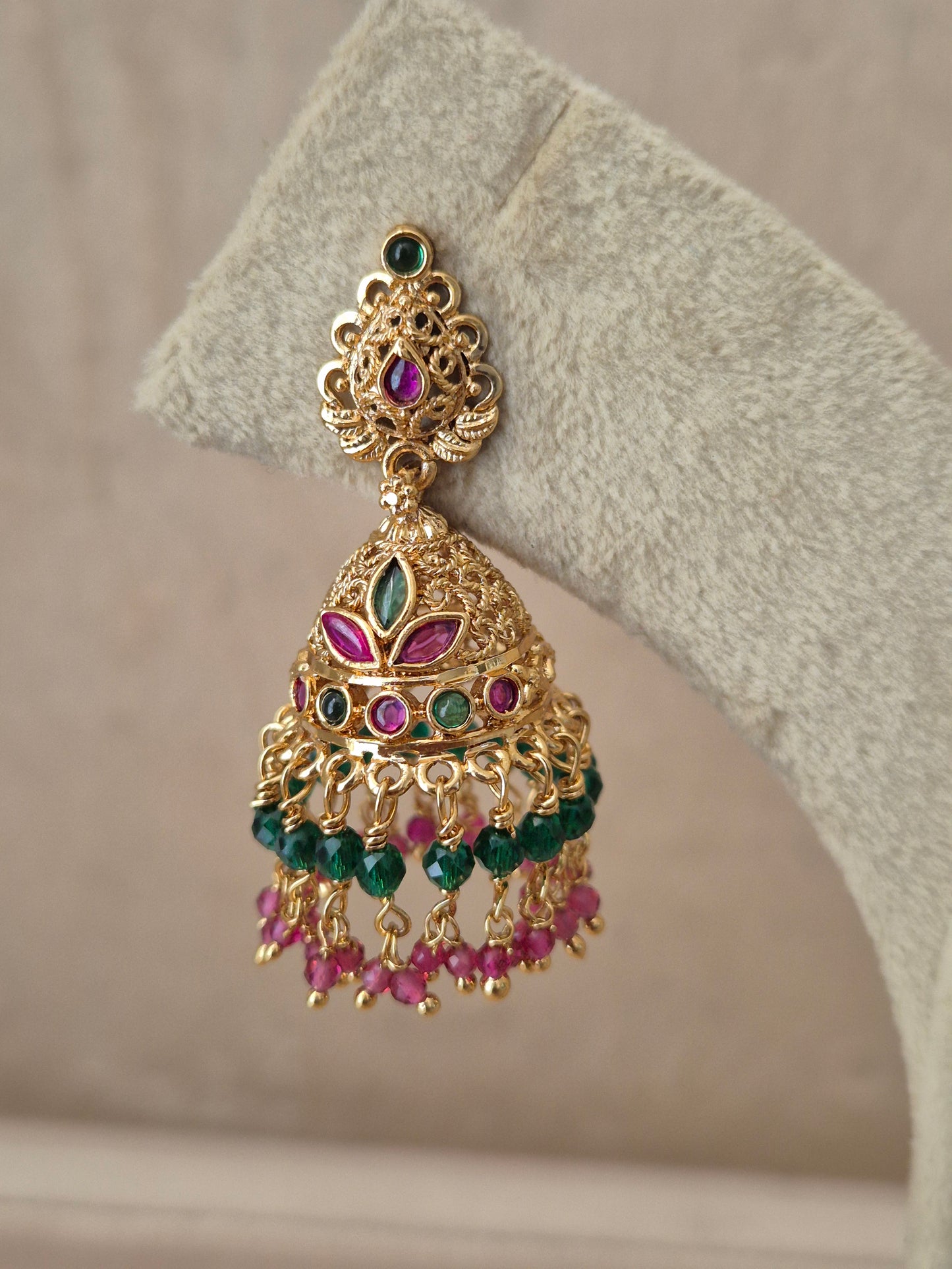Close-up of Naitri Anamika premium gold ethnic earrings showcasing traditional Indian temple jewelry craftsmanship with vibrant ruby red and emerald green stone embellishments by naitri.in