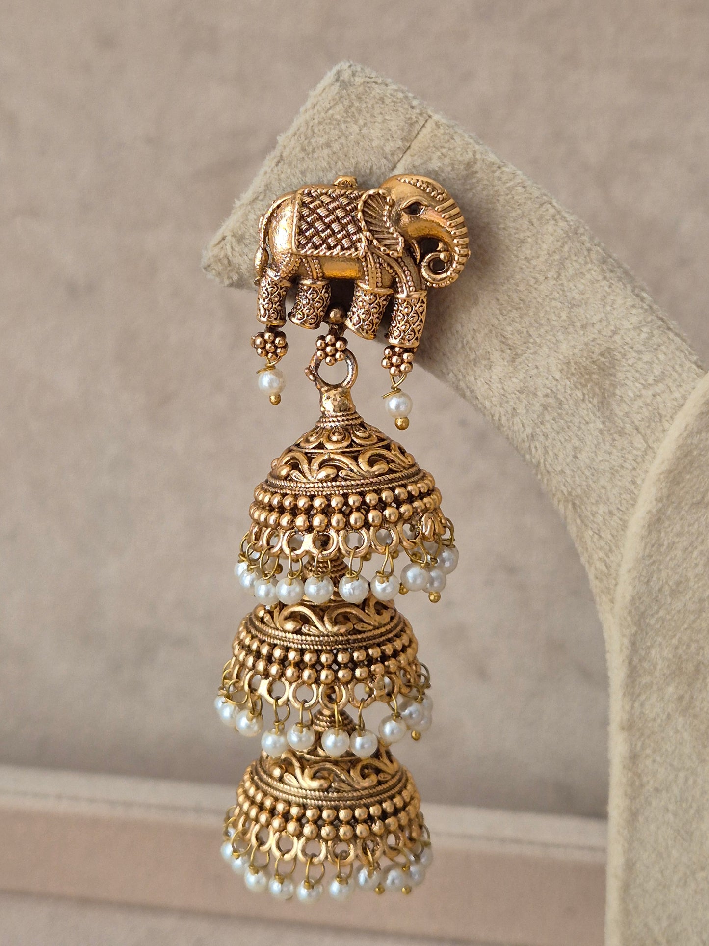 Gold-toned drop dangle earrings with intricate carved deity motifs, stone embellishments, and hanging pearl clusters by naitri.in