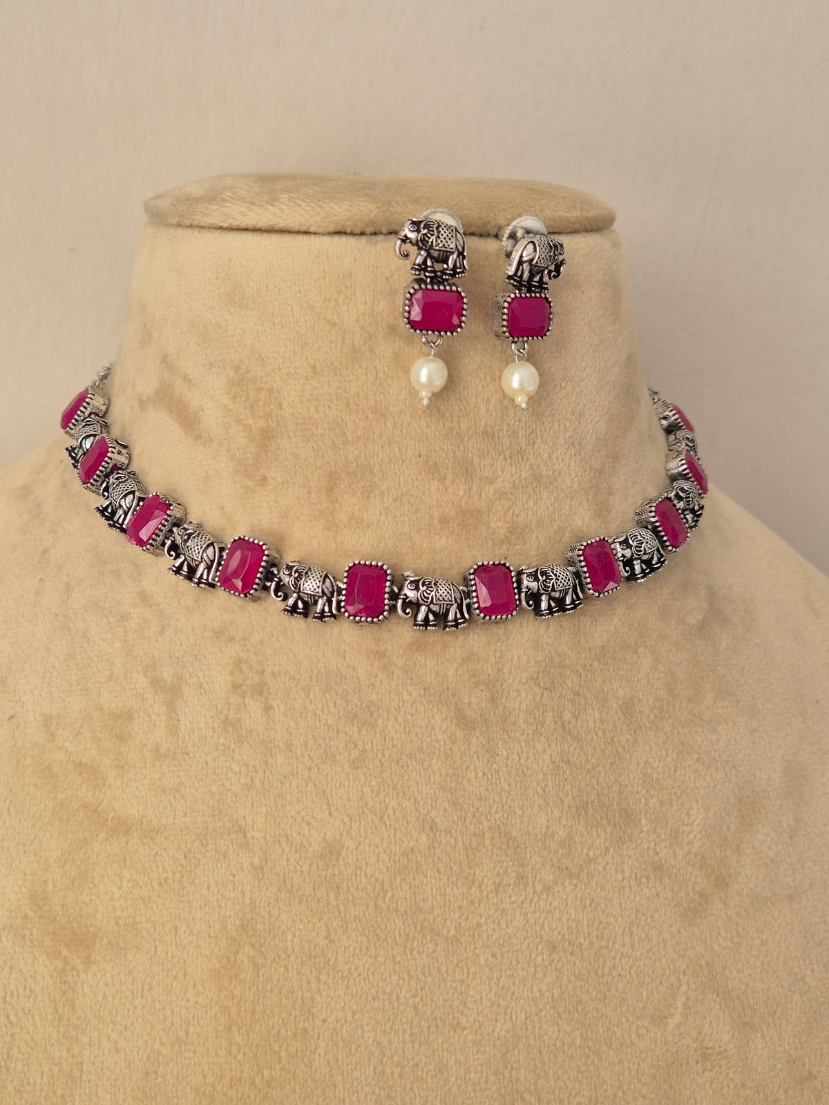 A matching jewelry set featuring a silver-toned chain necklace and matching drop earrings with bright pink rectangular stones and small white pearl-like drops by naitri.in