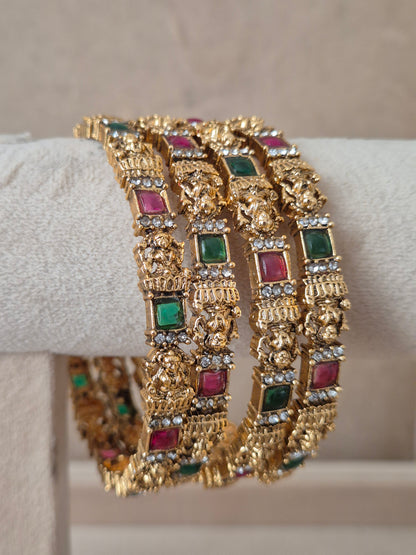 Close-up of Naitri Ashika premium gold ethnic bangle set with traditional Indian floral metalwork and vibrant red and green stone accents by naitri.in
