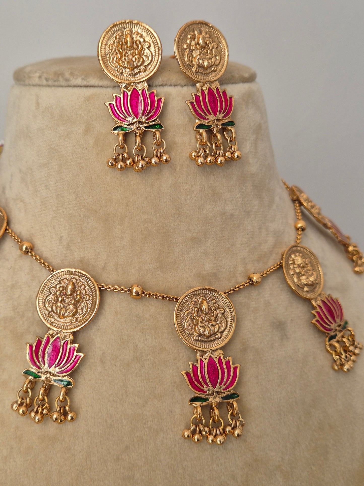Intricate golden choker necklace with circular deity pendants and vibrant pink lotus accents with matching earrings by naitri.in