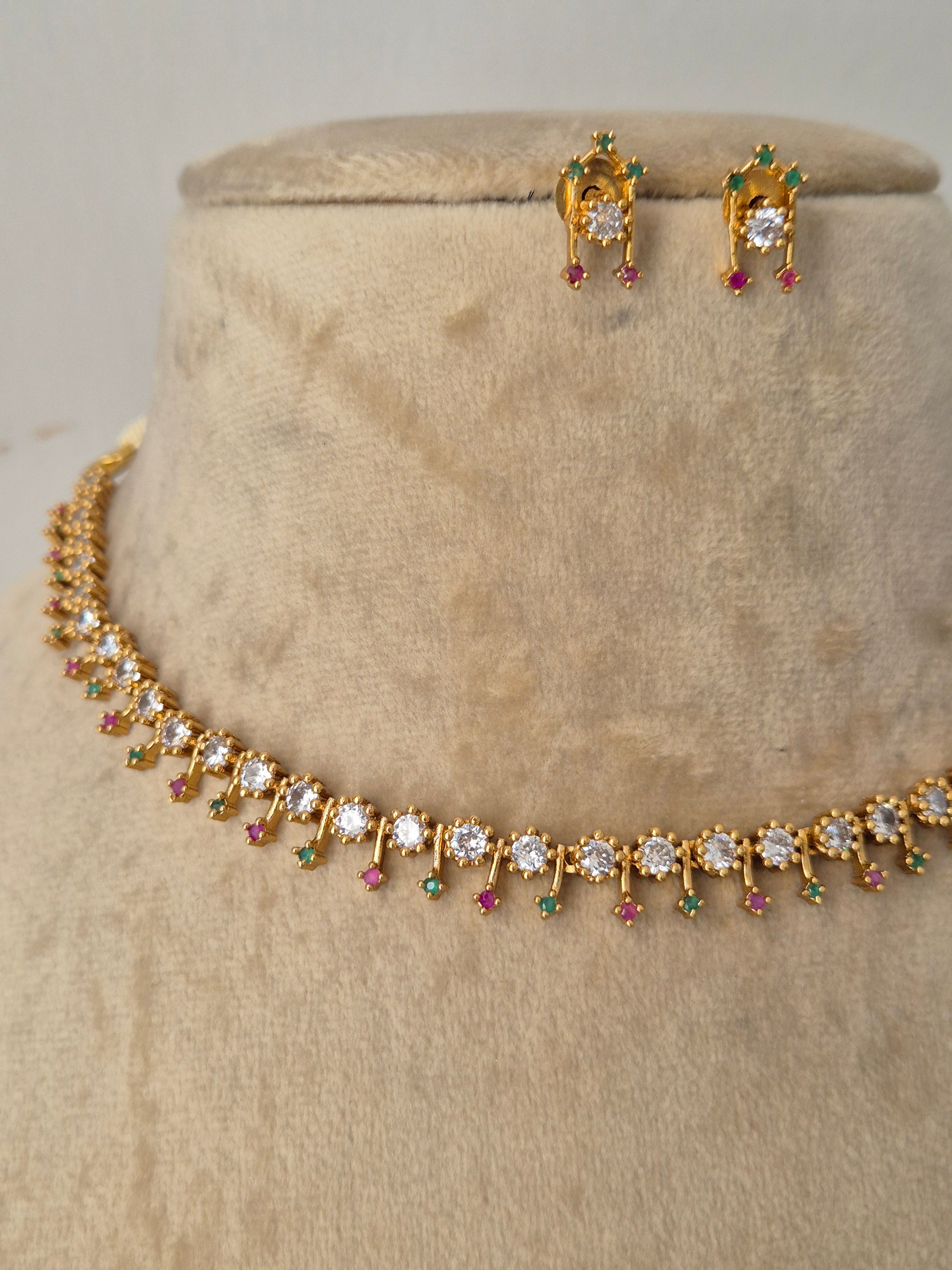 Minimalist gold-toned fine choker necklace adorned with a continuous row of delicate, dangling teardrop motifs in vibrant pinkish-red and sparkling clear crystals, shown with coordinating small drop earrings by naitri.in