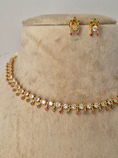 Minimalist gold-toned fine choker necklace adorned with a continuous row of delicate, dangling teardrop motifs in vibrant pinkish-red and sparkling clear crystals, shown with coordinating small drop earrings by naitri.in
