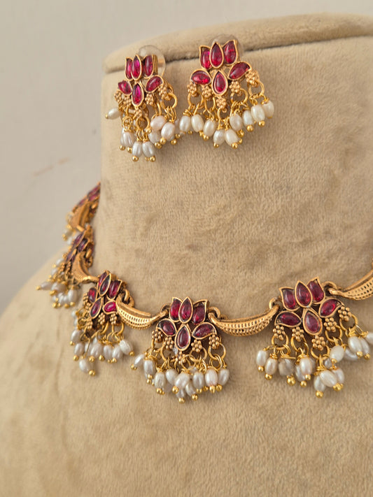 Gold-toned traditional jewelry set featuring a necklace and matching earrings, embellished with red stones and white pearl-like beads, by naitri.in