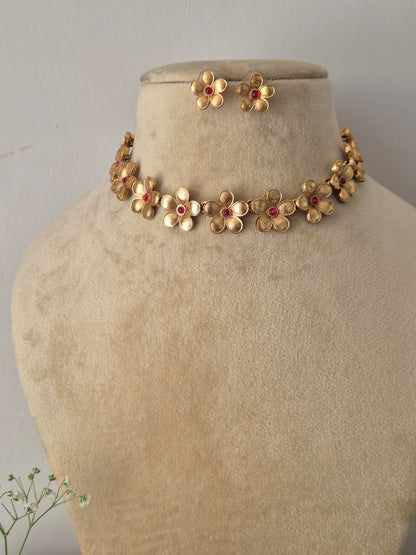 Modern Indian ethnic imitation jewelry set including a golden brass alloy choker necklace crafted with delicate floral motifs and pinkish-red stone centers, shown with matching flower earrings by naitri.in
