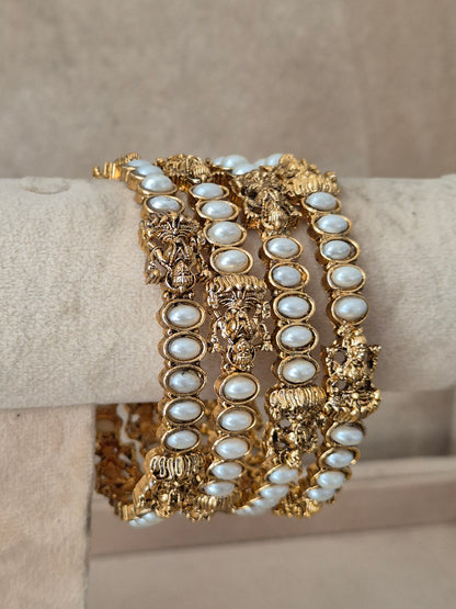 Set of four gold-plated bangles featuring intricate temple-style filigree work and embedded white pearls, by naitri.in
