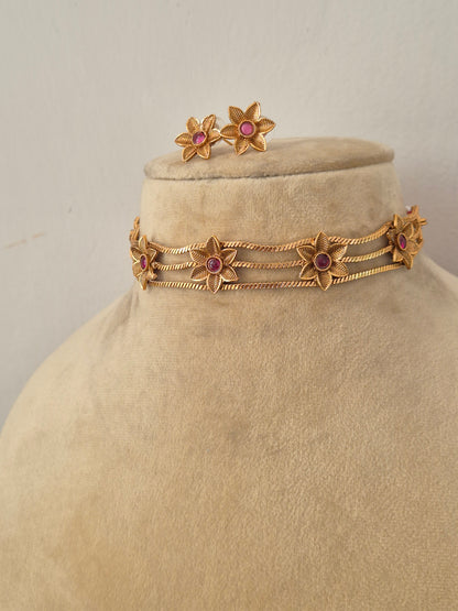 Modern Indian traditional imitation jewelry set including a golden brass alloy choker necklace with intricate cutout flower motifs and vibrant pink gemstones, by naitri.in