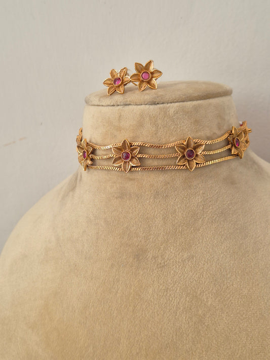 Modern Indian traditional imitation jewelry set including a golden brass alloy choker necklace with intricate cutout flower motifs and vibrant pink gemstones, by naitri.in