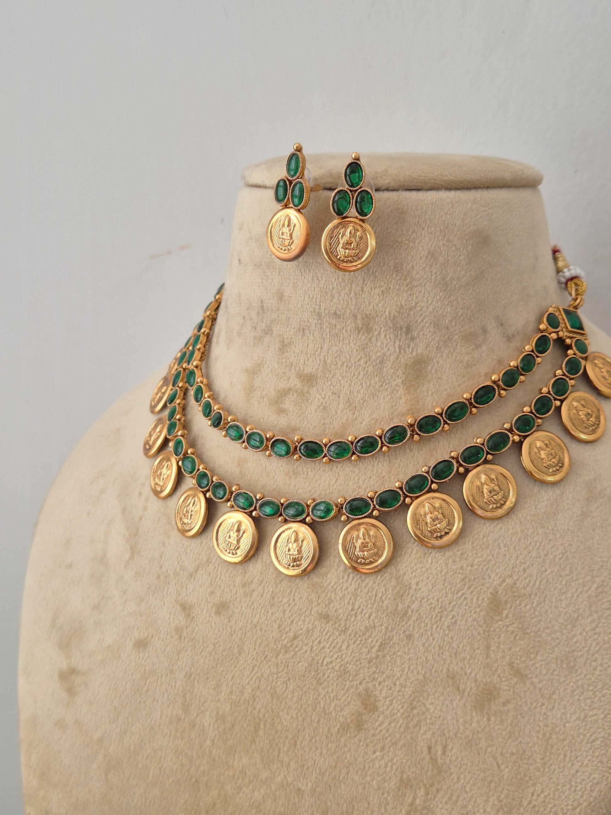 Indian-style golden coin necklace set with two rows of emerald green stones and matching drop earrings by naitri.in