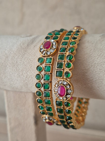 A gold-plated double-strand bangle bracelet decorated with green square and round stones and pink oval center stones, by naitri.in
