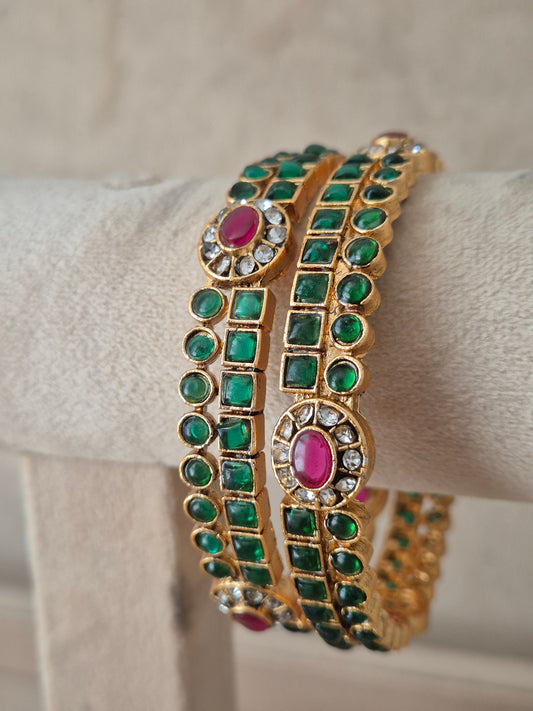 A gold-plated double-strand bangle bracelet decorated with green square and round stones and pink oval center stones, by naitri.in
