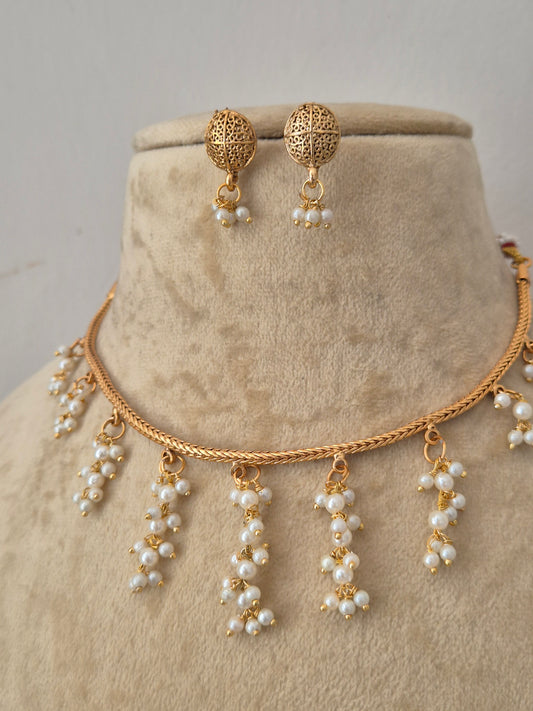 Gold-toned jewelry set including a choker necklace and matching drop earrings with pearl-like beads, necklace features a delicate chain designed with multiple dangling clusters of small white pearls, paired with matching textured round earrings that also feature hanging pearl droplets by naitri.in