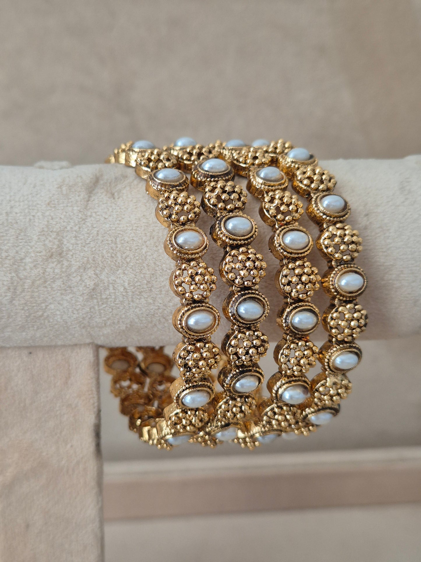 A wide gold-tone cuff bracelet with multiple rows of oval white pearl-like stones set in textured floral clusters, by naitri.in