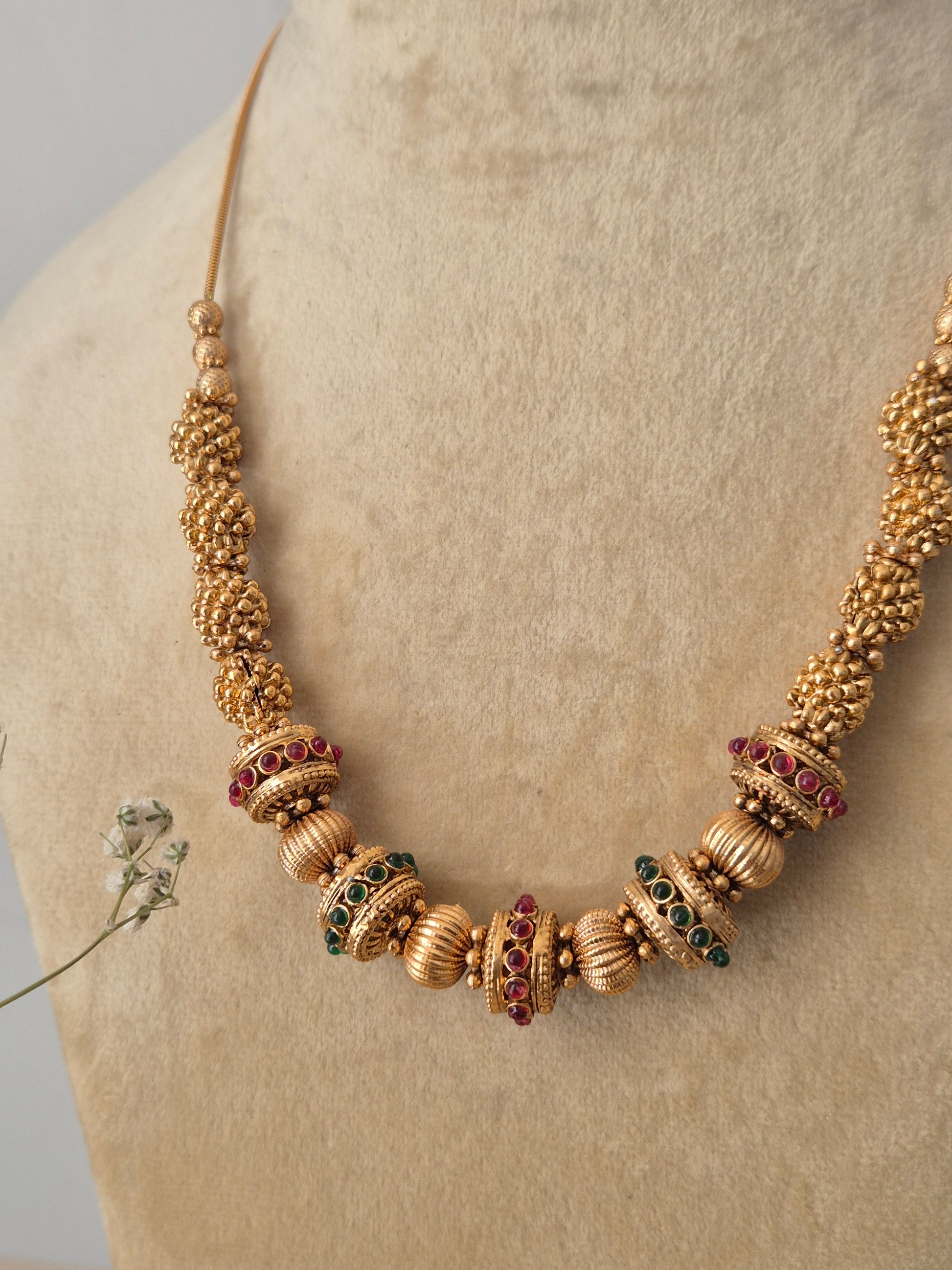 Traditional Devi necklace made from brass alloy with a polished golden finish, showcasing a snake chain design with textured gold spacers and ruby-red stone details by naitri.in
