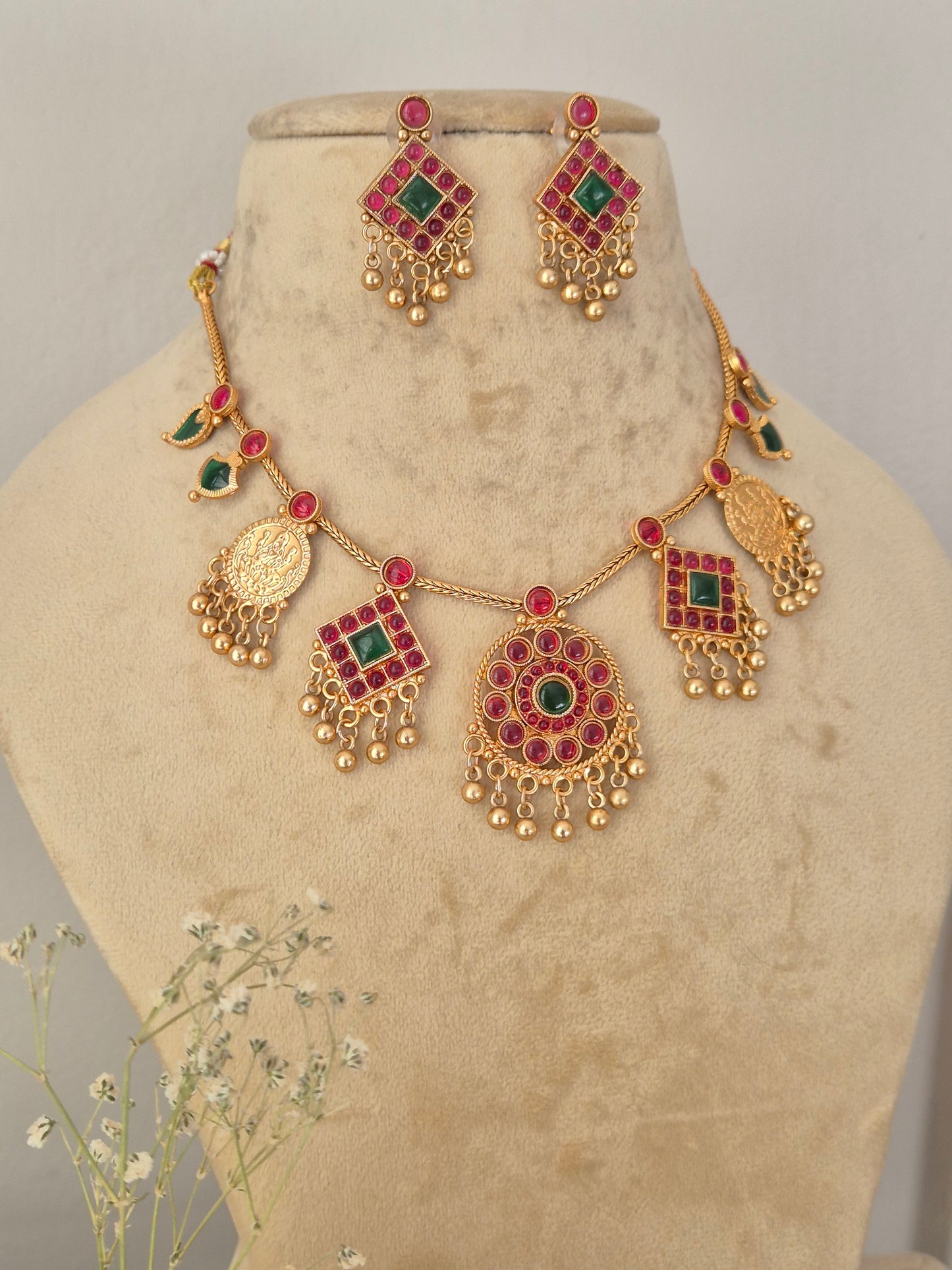 Gold-toned traditional Indian jewelry set including a necklace, earrings, and a bracelet, embellished with red and green stones, by naitri.in