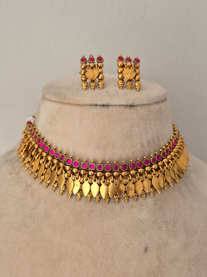 Gold-toned traditional jewelry set including a choker necklace with dangling leaf-shaped charms, matching earrings, and small pink stones throughout by naitri.in