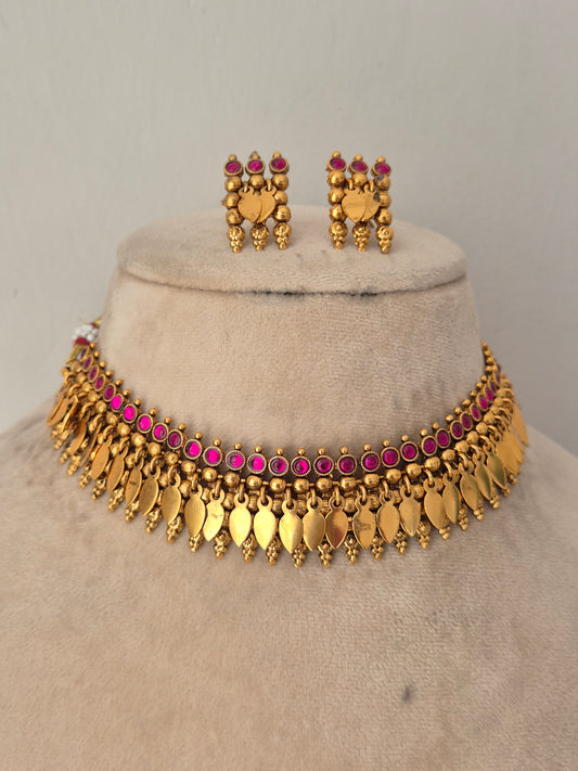 Gold-toned traditional jewelry set including a choker necklace with dangling leaf-shaped charms, matching earrings, and small pink stones throughout by naitri.in