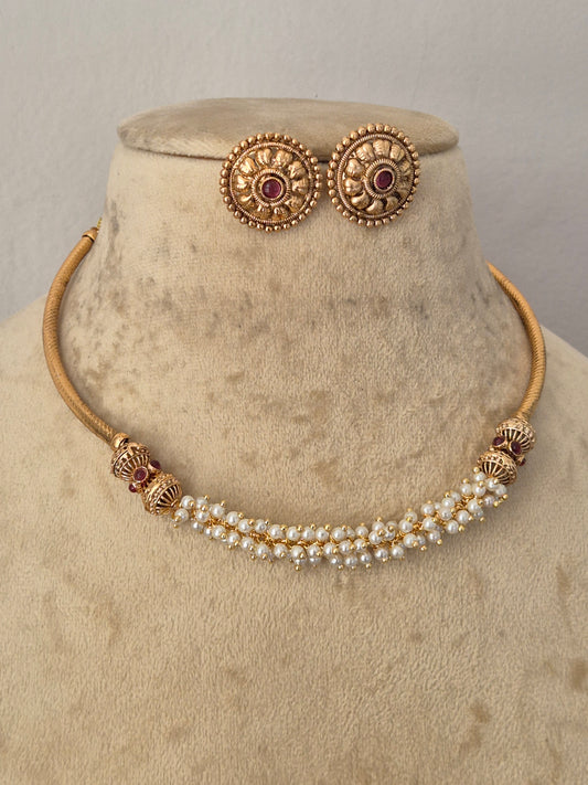 Gold-plated traditional Indian jewelry set featuring a double-row pearl necklace with gold-toned decorative beads and a matching pair of round stud earrings with red gemstone centers, by naitri.in