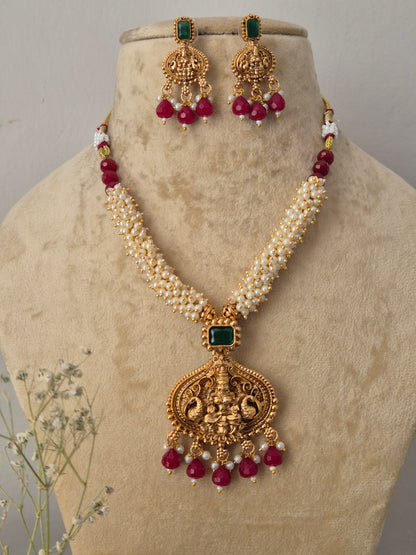 Gold-plated traditional Indian jewelry set featuring a necklace and matching earrings with cream-colored faux pearls, green stone accents, and deep red bead drops, by naitri.in