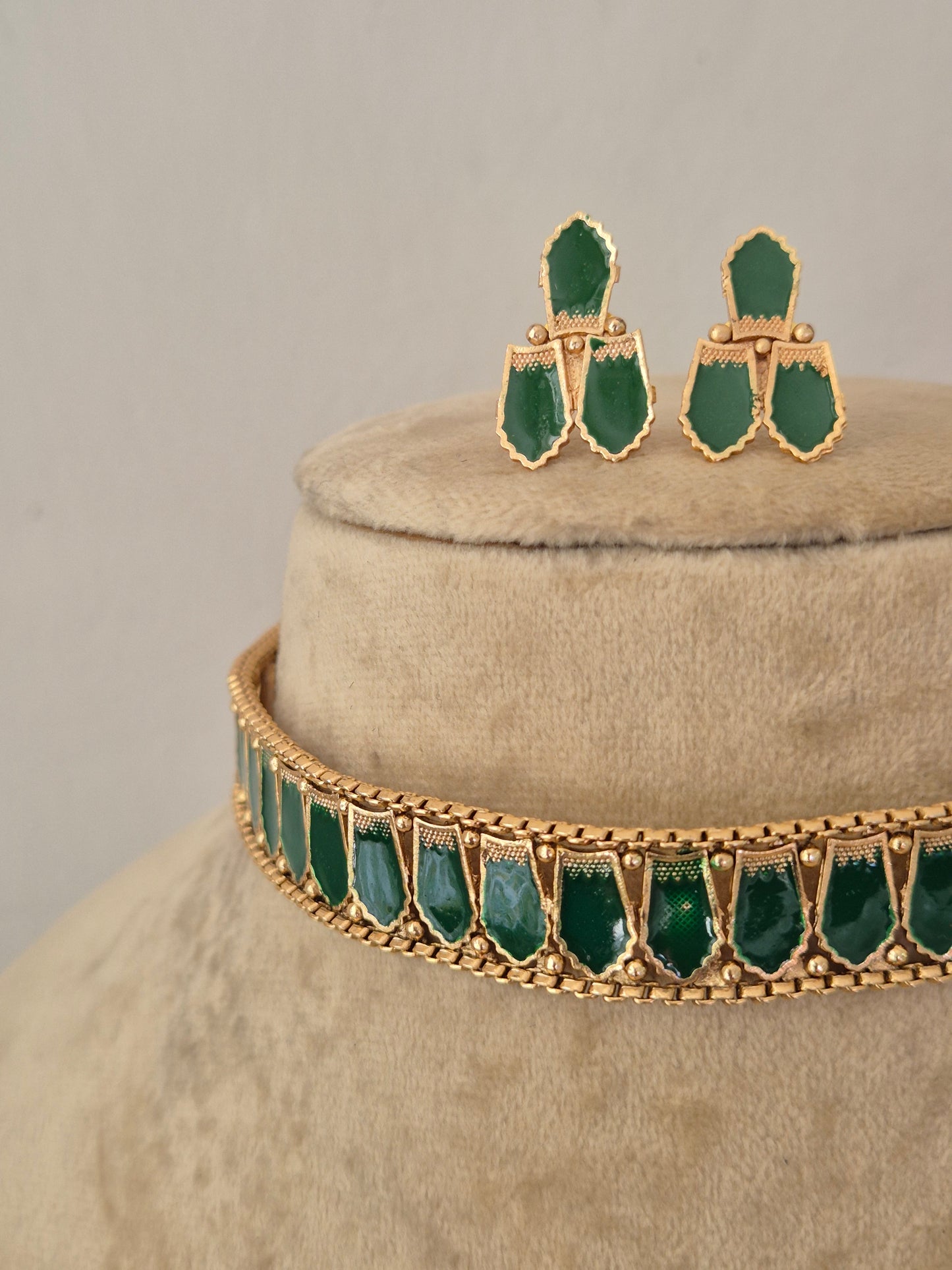 Gold-toned jewelry set featuring a choker necklace and matching drop earrings, both decorated with green teardrop-shaped stones, by naitri.in