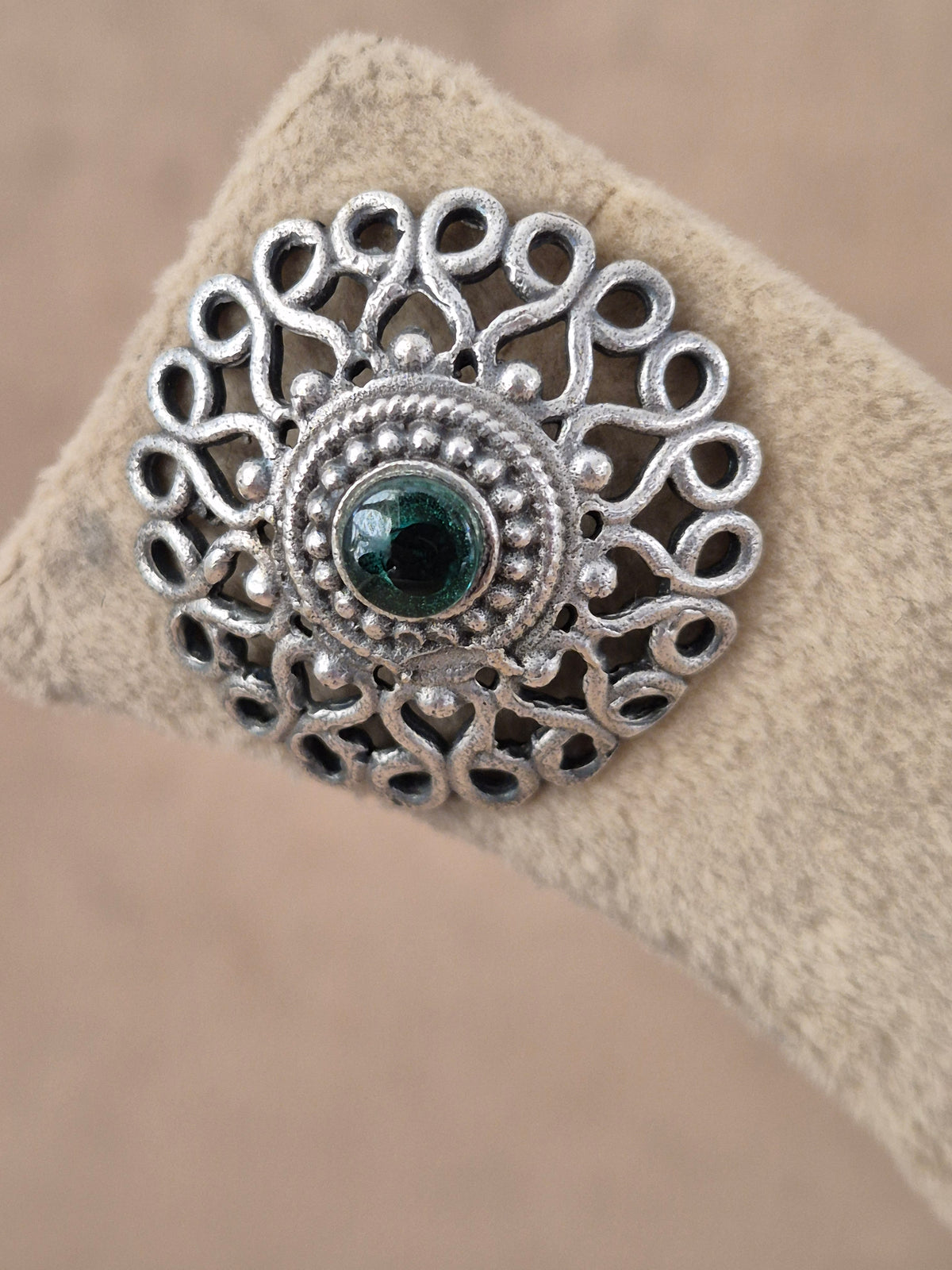 A close-up of a silver filigree ring with a central dark green gemstone, by naitri.in