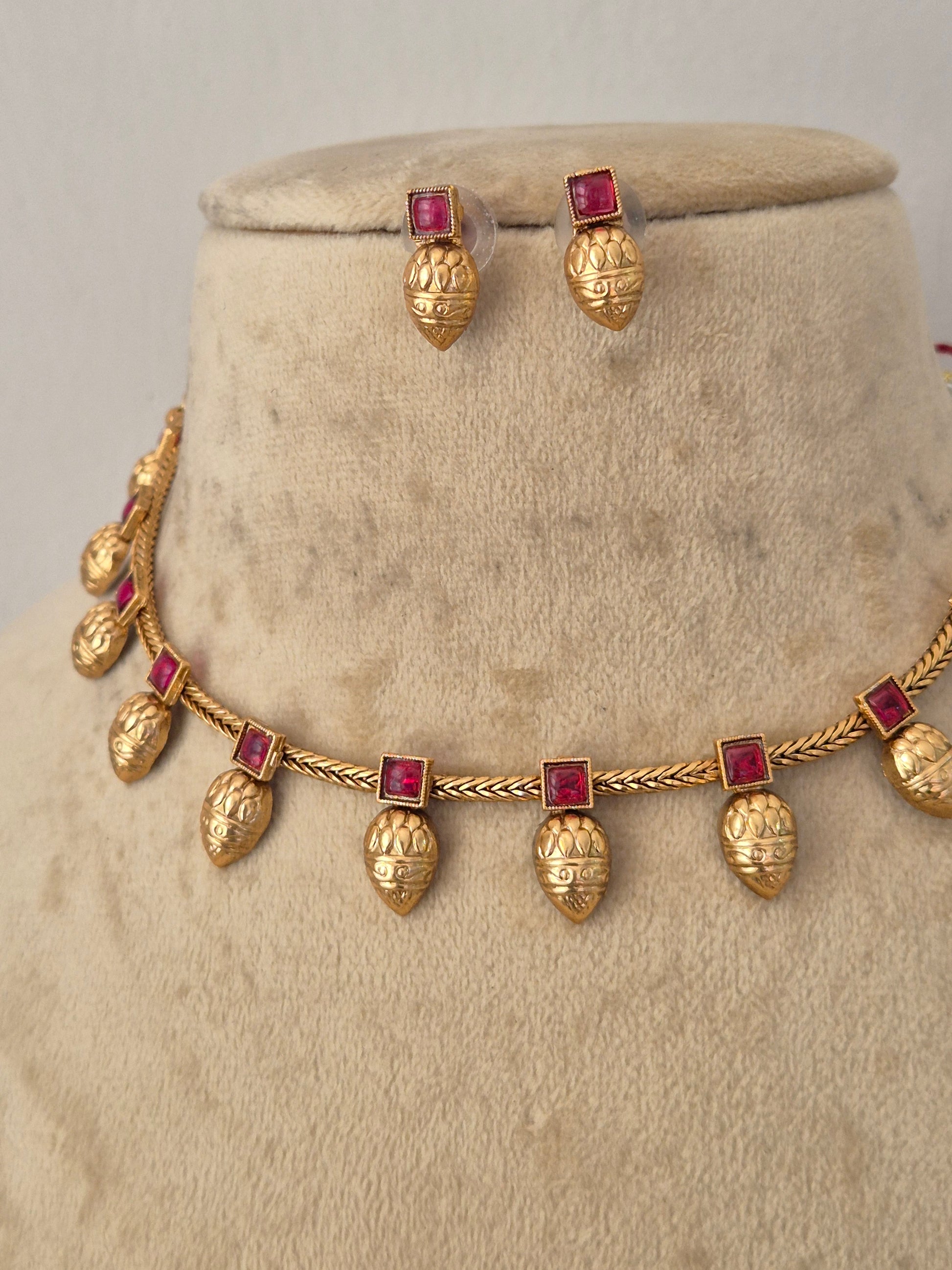 Gold jewelry set featuring a necklace and matching earrings with textured gold leaf pomegranate-shaped charms and square red gemstone accents, by naitri.in