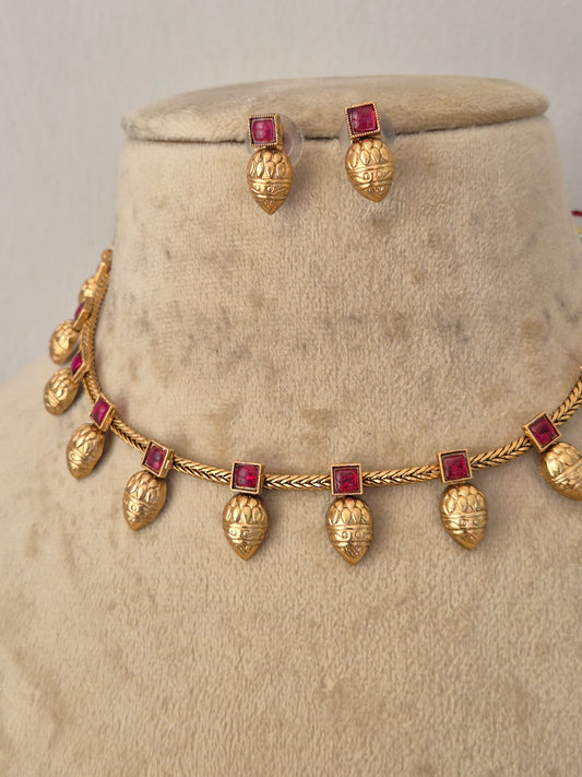 Gold jewelry set featuring a necklace and matching earrings with textured gold leaf pomegranate-shaped charms and square red gemstone accents, by naitri.in