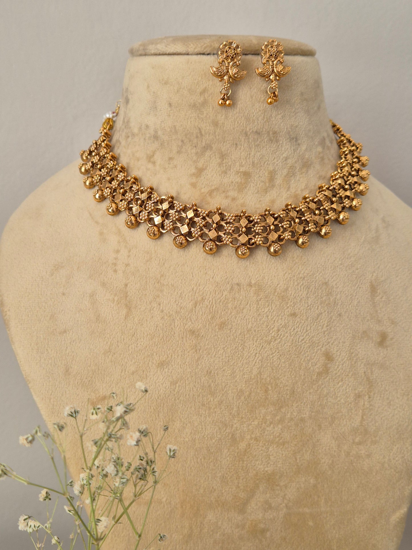 Traditional gold-toned choker necklace and drop earrings set with an intricate textured design and hanging bead details by naitri.in