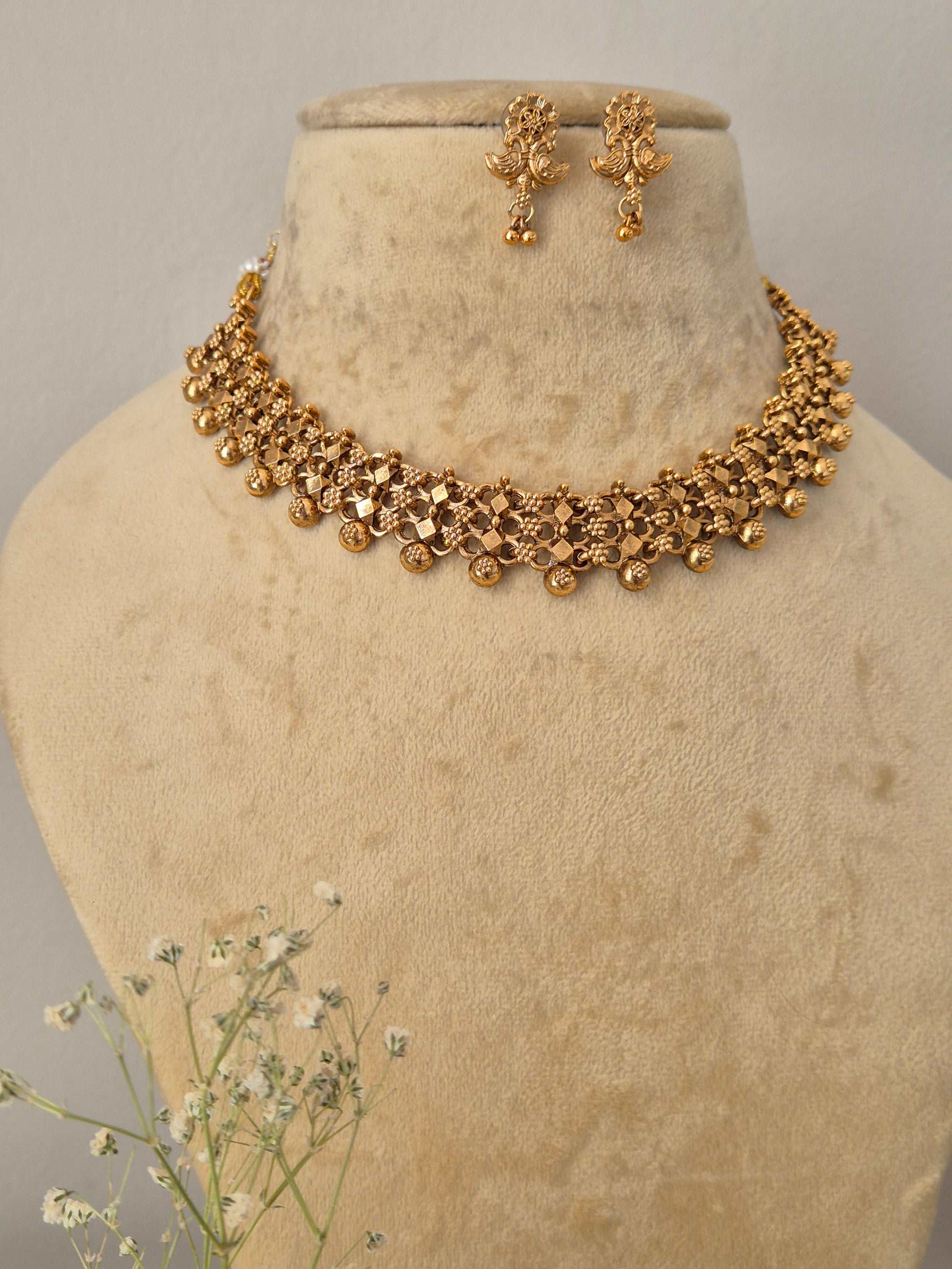 Traditional gold-toned choker necklace and drop earrings set with an intricate textured design and hanging bead details by naitri.in