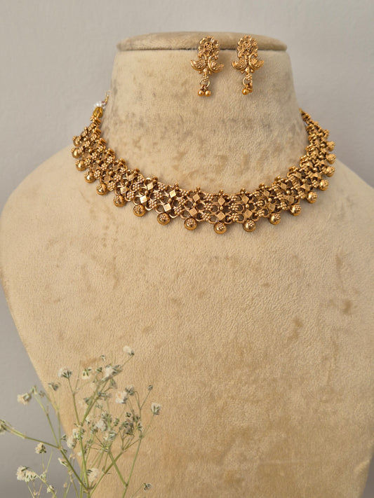 Traditional gold-toned choker necklace and drop earrings set with an intricate textured design and hanging bead details by naitri.in