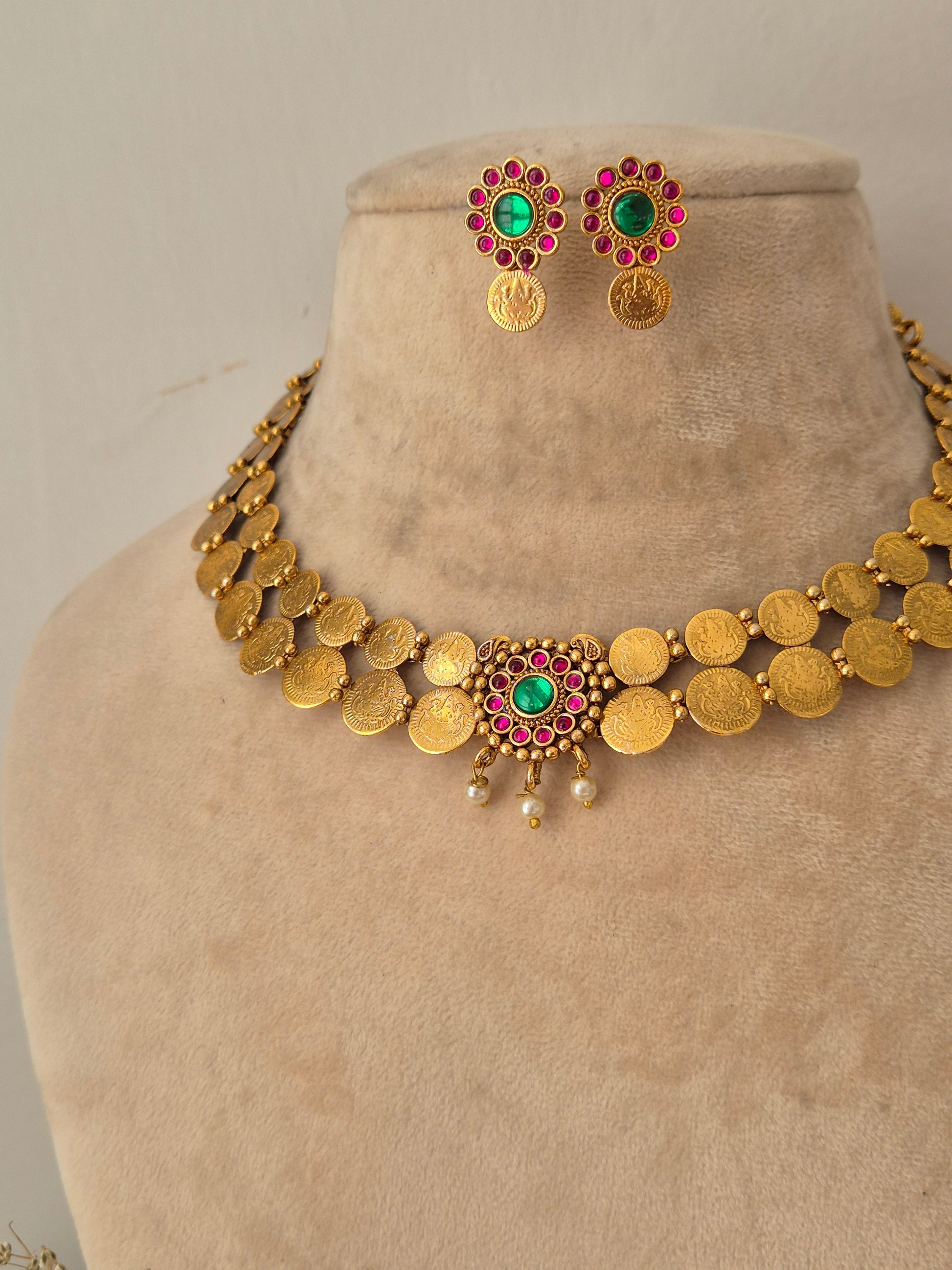 Gold-toned coin necklace featuring a central green stone pendant, red stone accents, hanging pearls, and matching round stud earrings by naitri.in