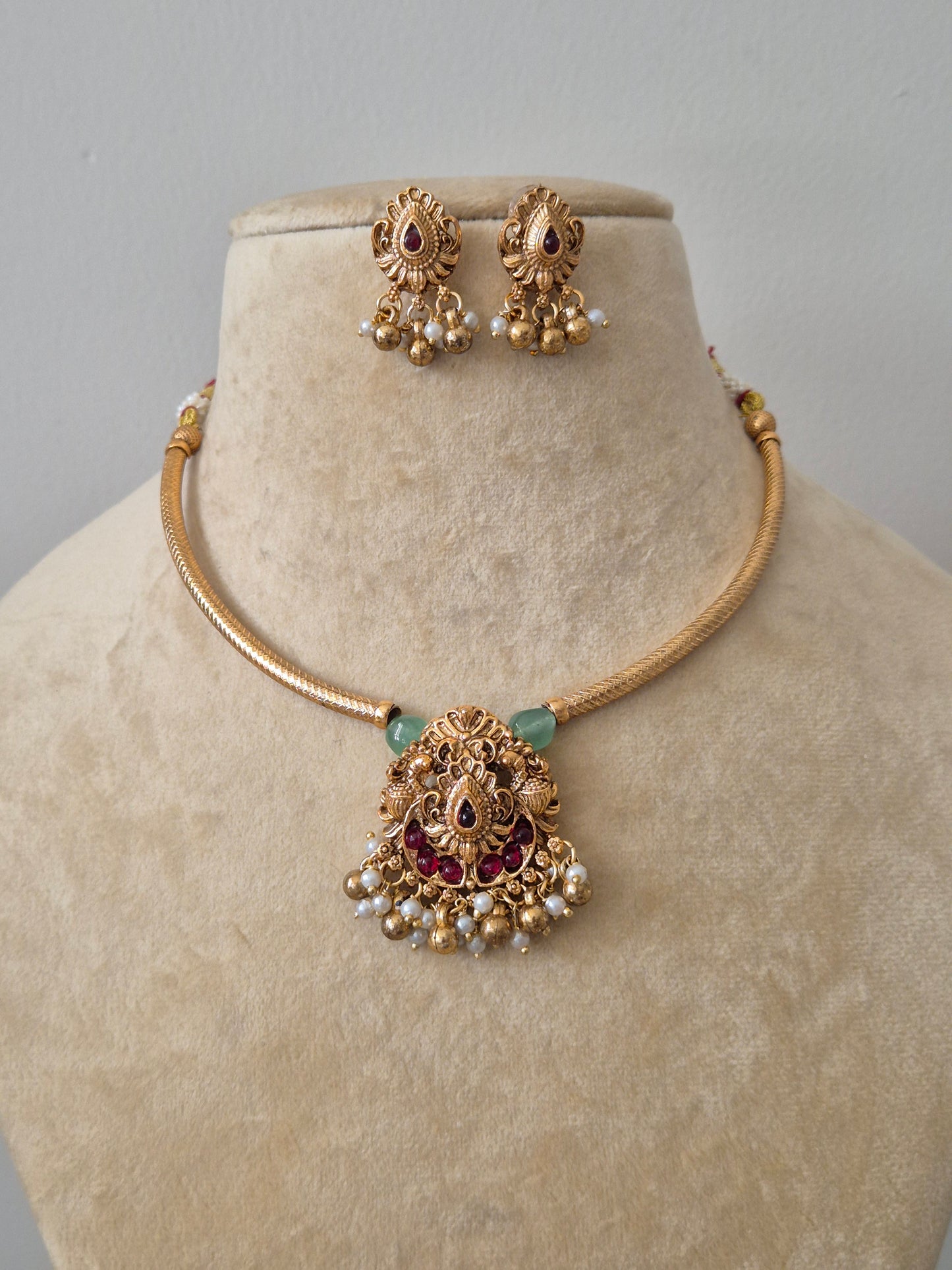 Traditional gold temple necklace set with pink and green stones and pearl droplets, including matching jhumka earrings by naitri.in