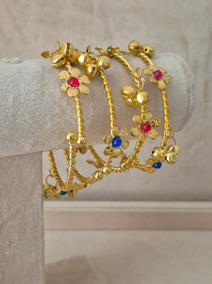 Close-up of Naitri Geetanjali premium gold ethnic bangles showcasing traditional Indian floral craftsmanship with colorful gemstone accents and elegant hanging latkan charms by naitri.in