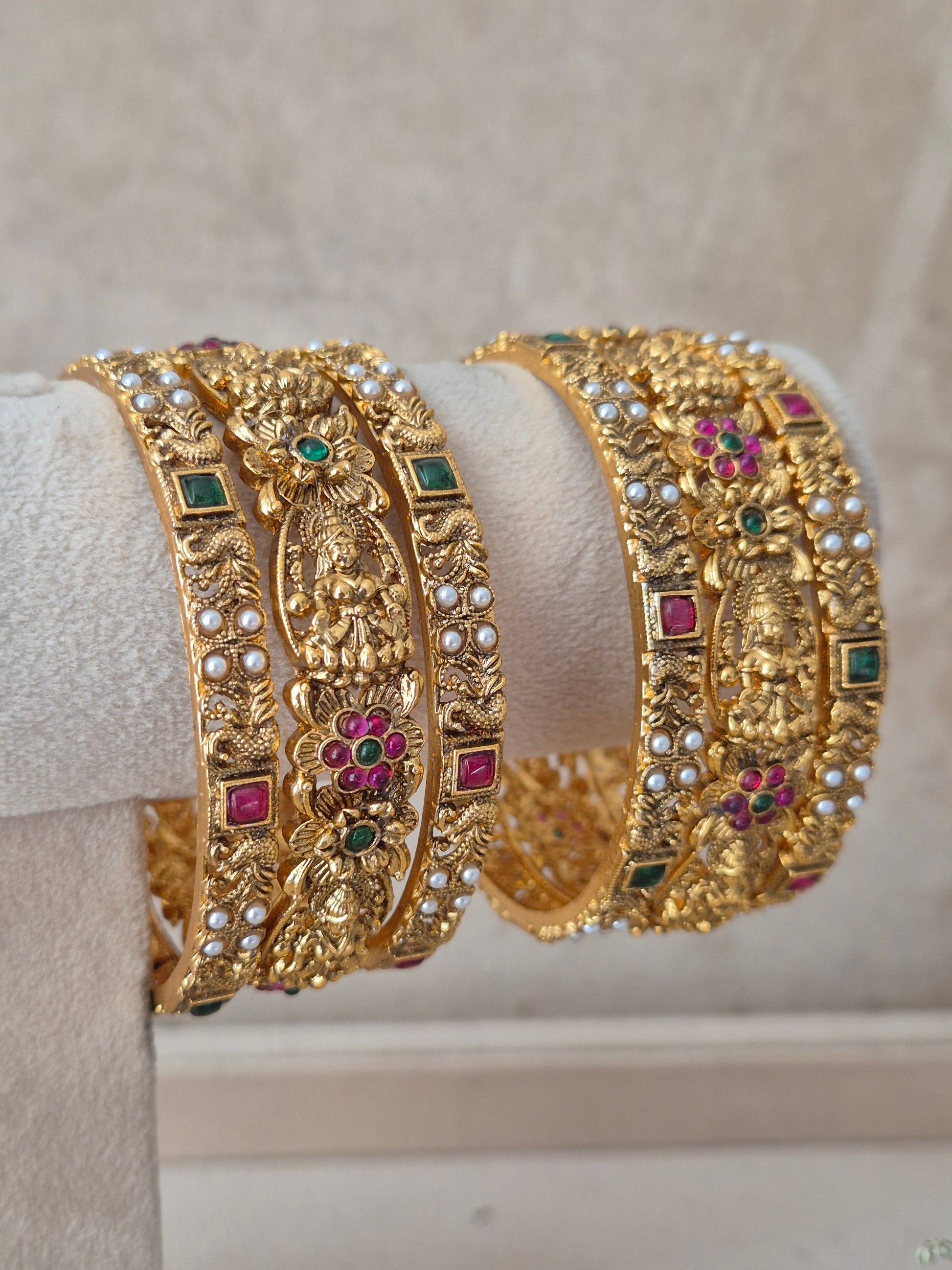 Set of 6 gold-toned antique temple bangles featuring intricate goddess motifs, studded with green and ruby-red stones, accents for bridal and ethnic wear by naitri.in