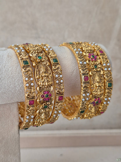 Set of 6 gold-toned antique temple bangles featuring intricate goddess motifs, studded with green and ruby-red stones, accents for bridal and ethnic wear by naitri.in