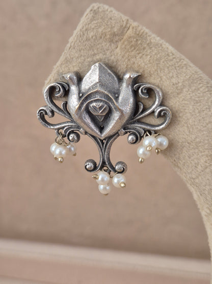 An ornate silver-toned brooch featuring two birds and dangling pearl beads, by naitri.in