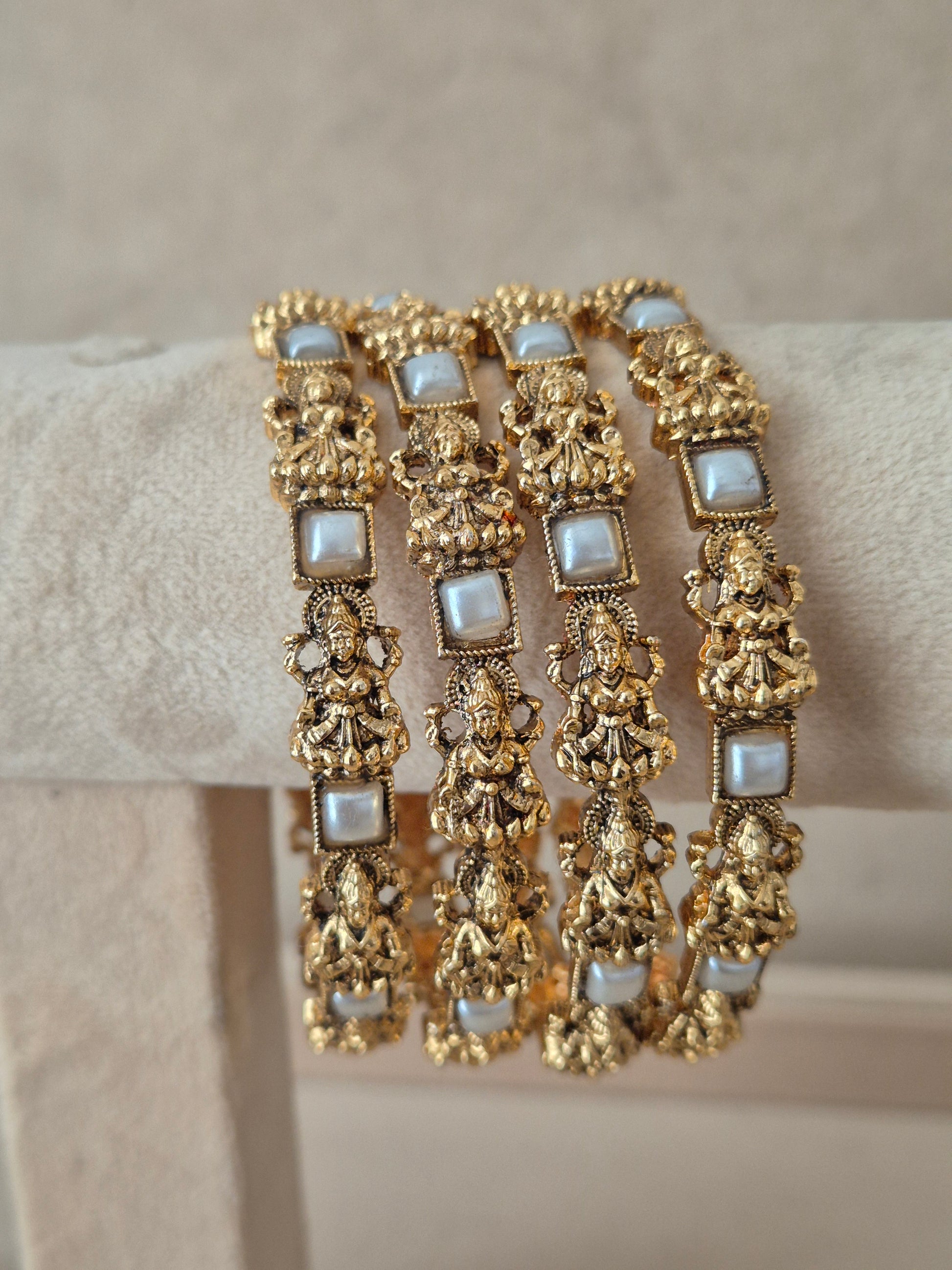 A stack of four traditional Indian antique gold-plated bangles set with intricate deity motif carvings and decorated  square white stone accents, by naitri.in